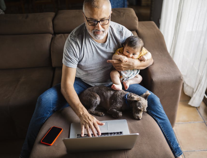 Grandpa with baby & puppy snuggled in his lap, while taking care on business on laptop