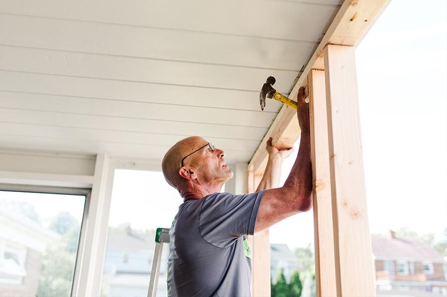 Man holding wooden board up while holding a hammer
